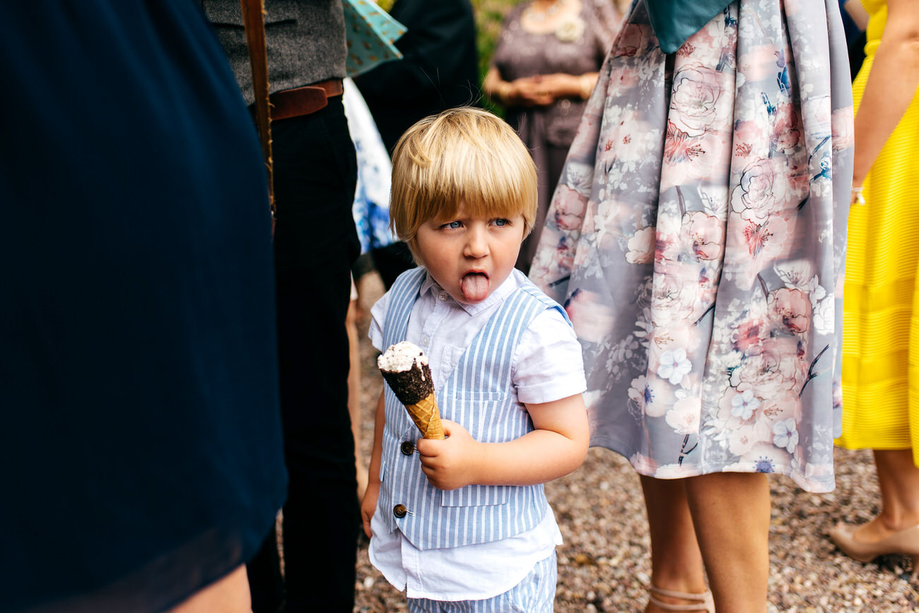 Boy with tongue out and ice cream in his hand on a hot summers wedding day 