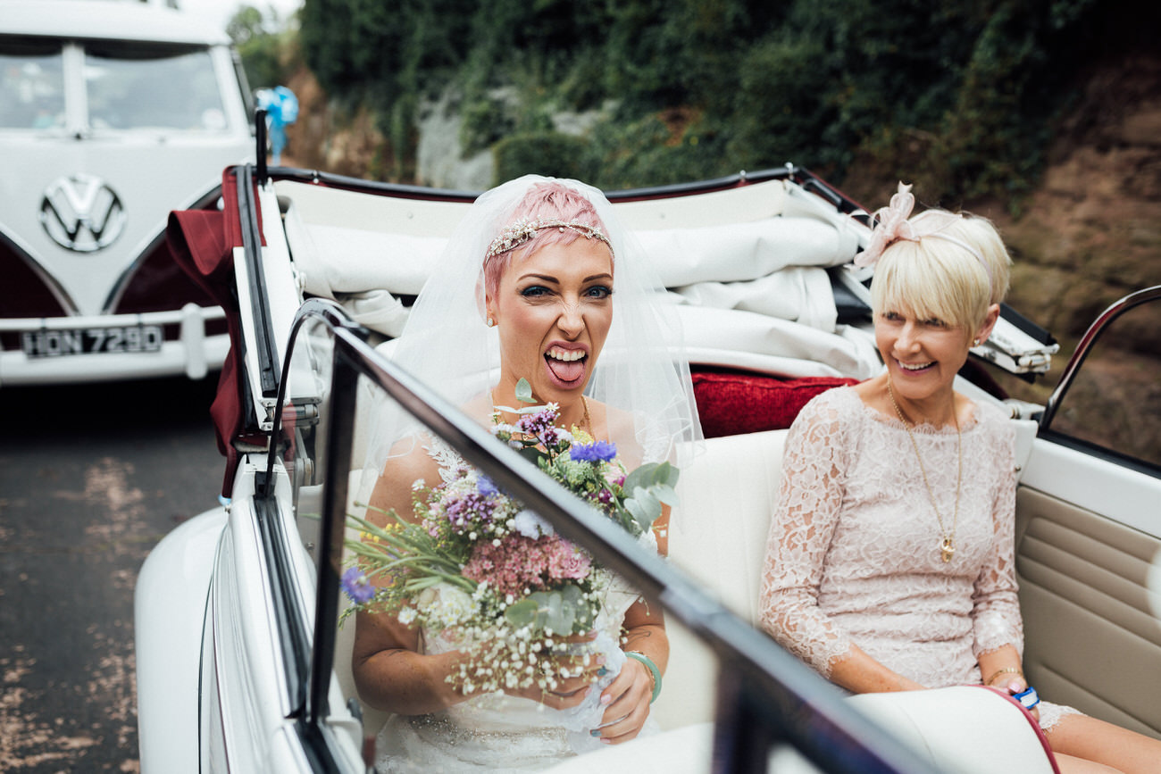 Pink haired bride in VW Beetle sticking her tongue out with mum laughing