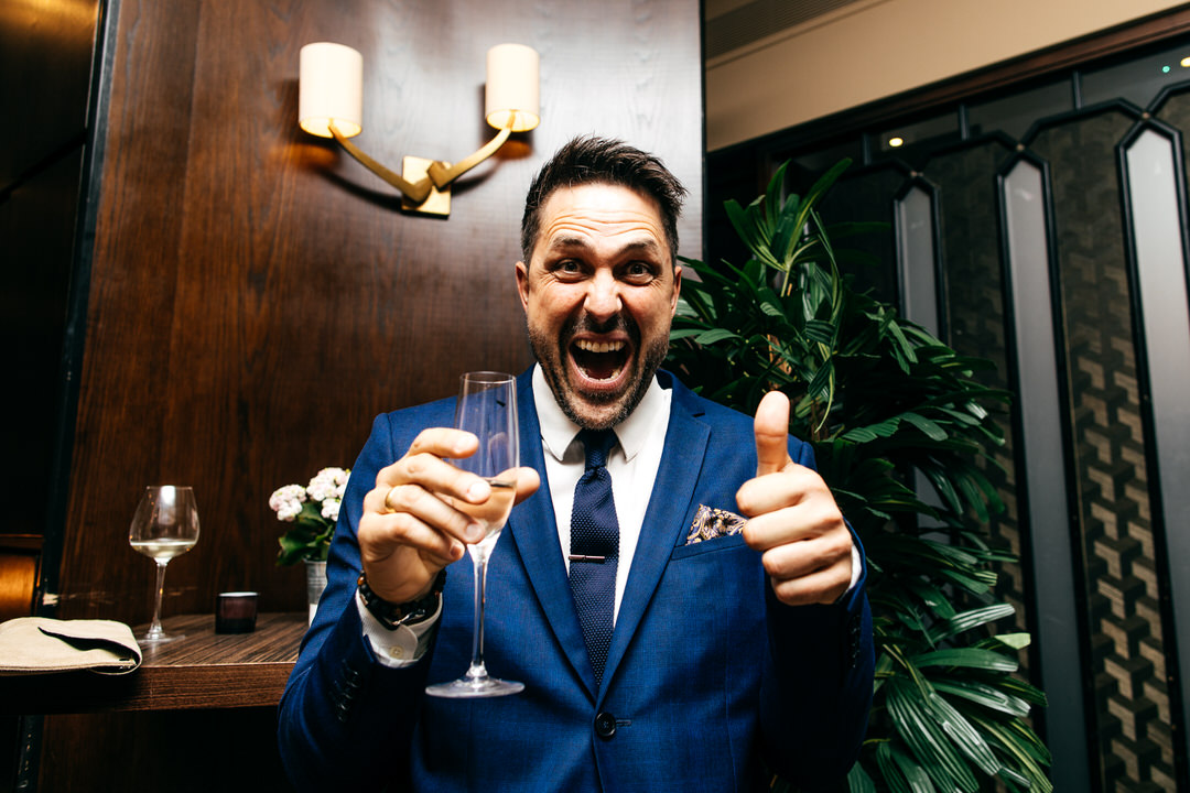 funny-guest-blue-suit-gives-thumbs-up-holding-champagne